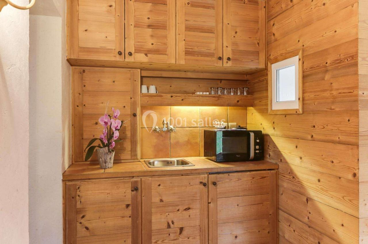 Cuisine compacte en bois avec évier, micro-ondes, étagères ouvertes et une orchidée décorative sur le plan de travail.