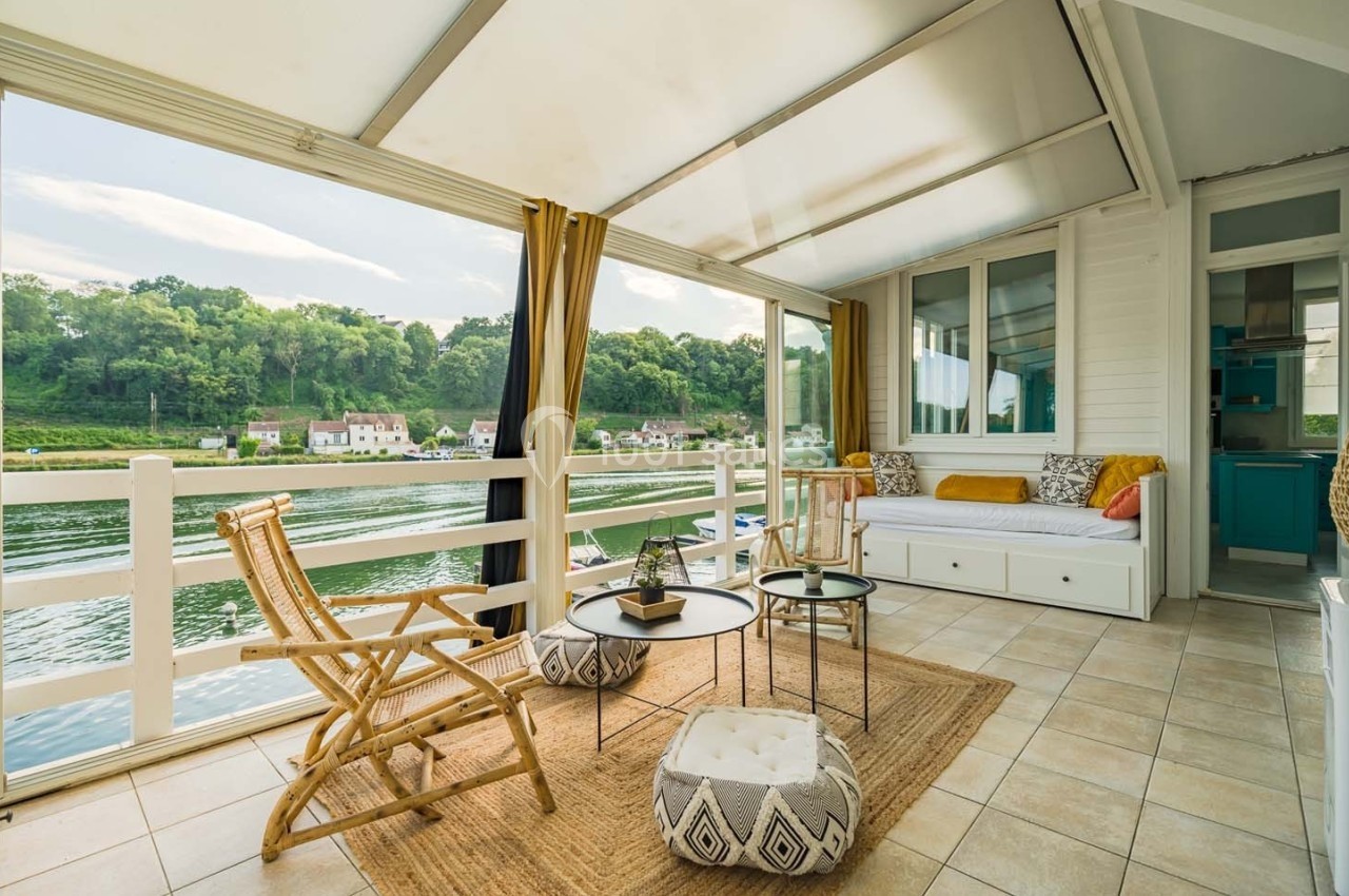 Salon lumineux avec vue sur une rivière, aménagé avec des fauteuils en rotin, une banquette et des tables basses.