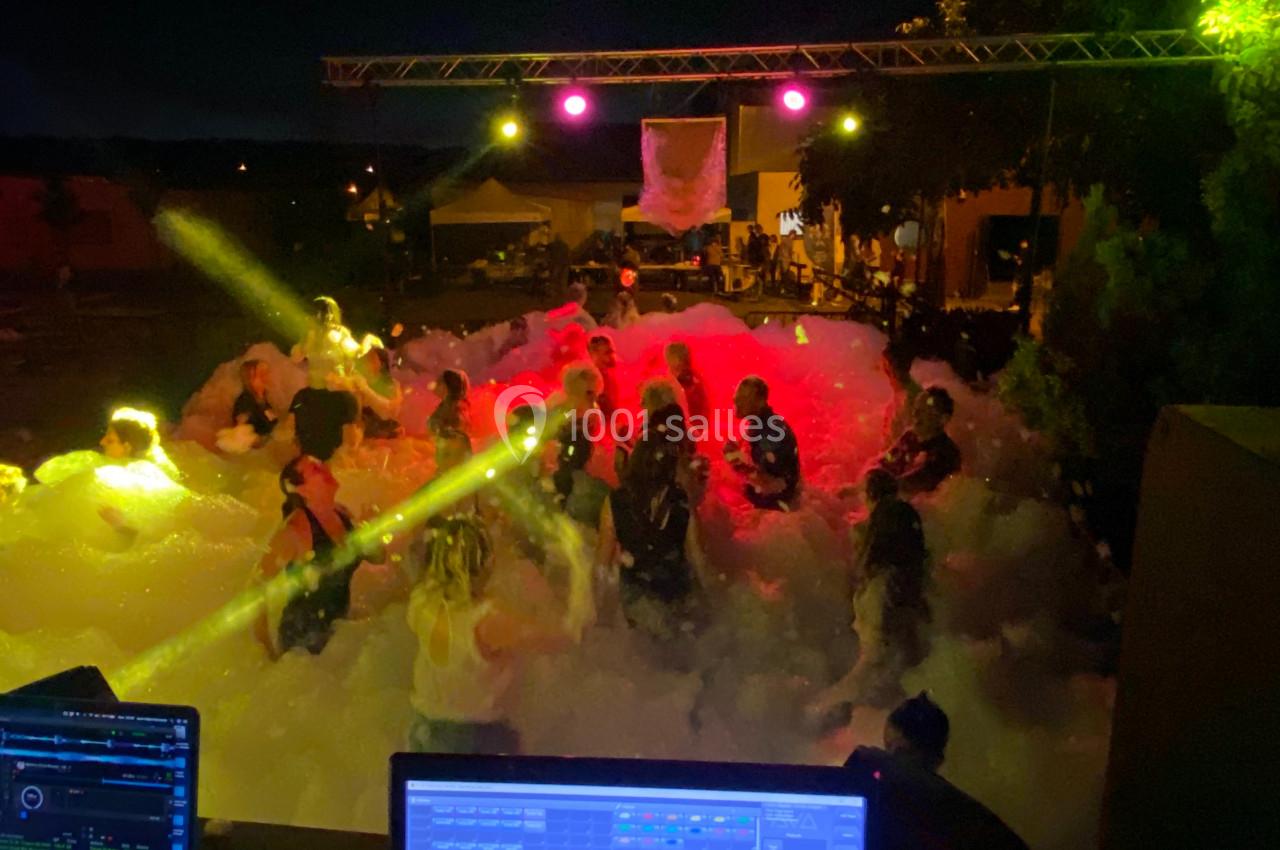 Des personnes dansent de nuit dans une ambiance festive avec des lumières colorées et une grande quantité de mousse.