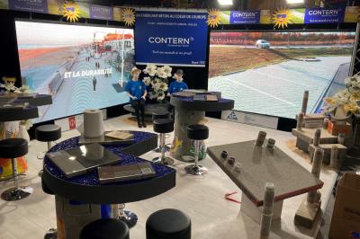 Stand d'exposition présentant des produits en béton, avec écrans, échantillons et décorations sur des tables.