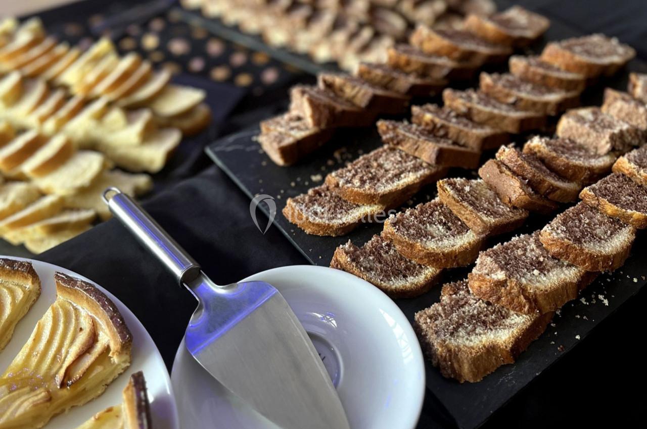 Tranches de brioche et de tarte aux pommes disposées sur une table noire, avec une pelle à tarte en premier plan.