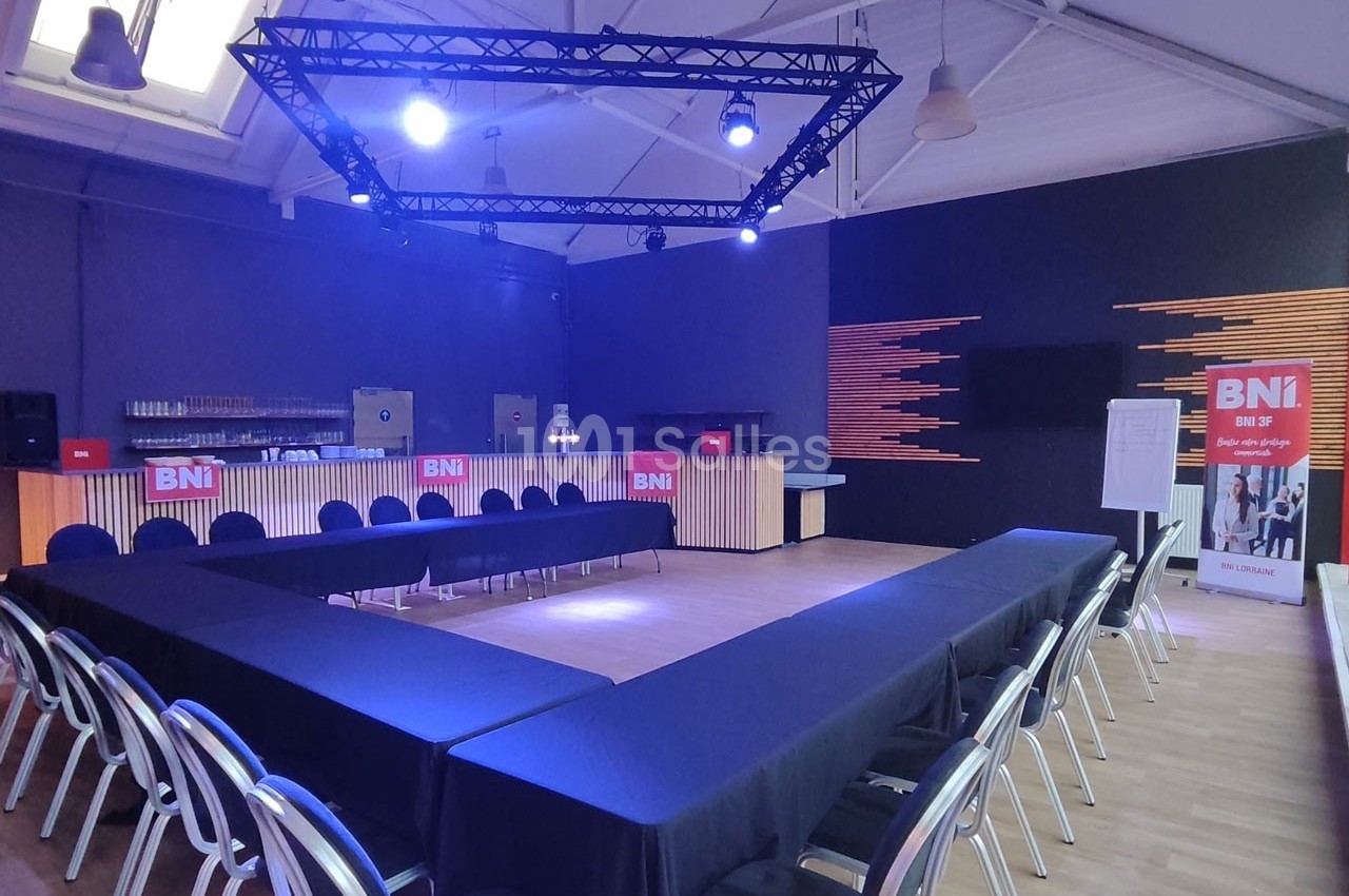 Salle de réunion avec tables disposées en U, chaises alignées, éclairage bleu et panneaux ’BNI’ en arrière-plan.