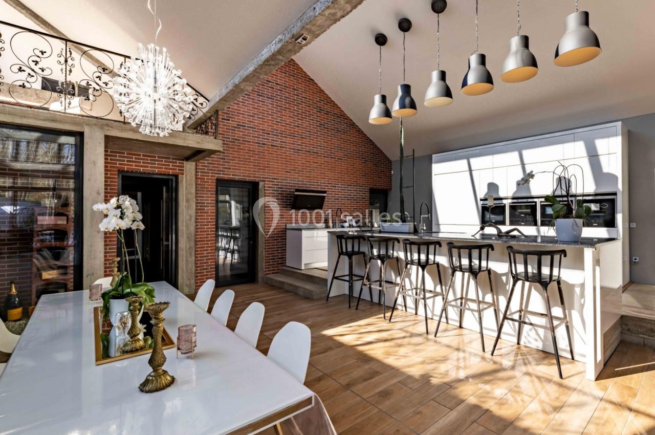 Cuisine ouverte moderne avec îlot central, table à manger design, murs en briques et luminaires suspendus.