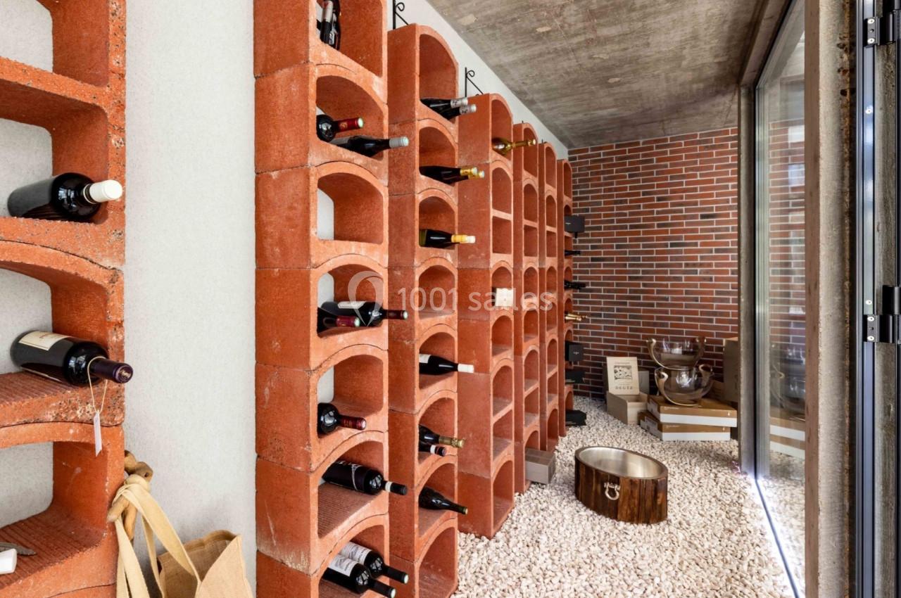 Cave à vin avec étagères en briques rouges, bouteilles rangées et sol recouvert de gravier blanc.