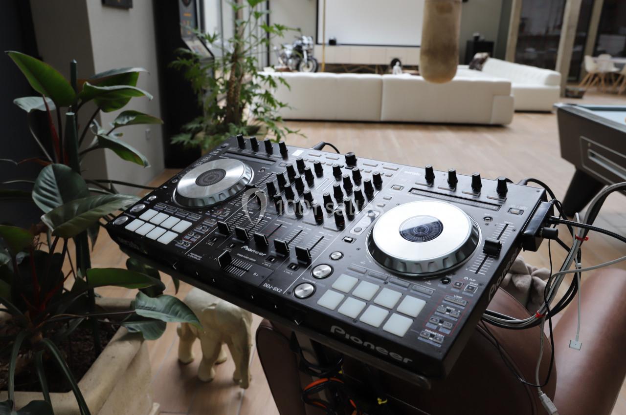 Table de mixage DJ avec platines et boutons, installée dans un espace intérieur lumineux avec des plantes et des meubles.