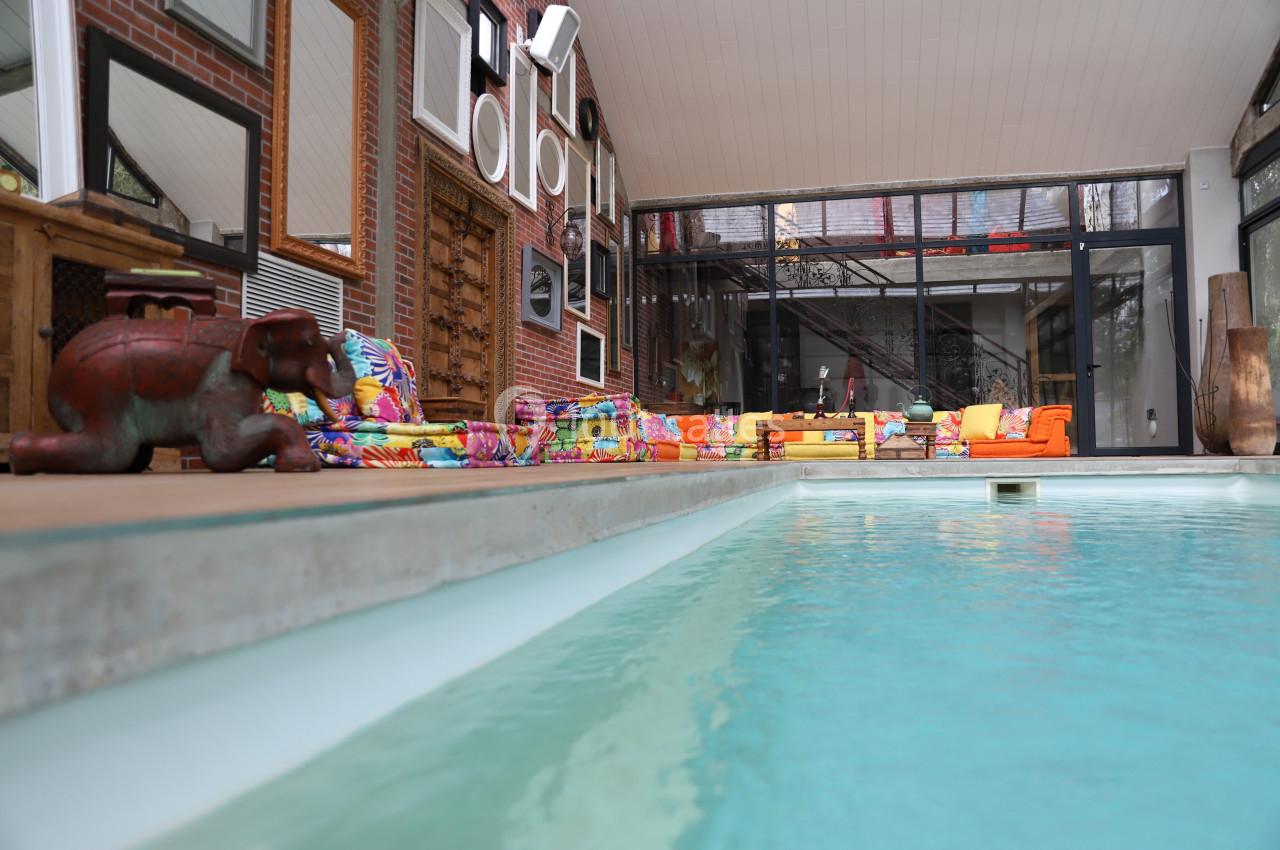 Piscine intérieure bordée de mobilier coloré et de décorations murales dans un espace lumineux avec baies vitrées.