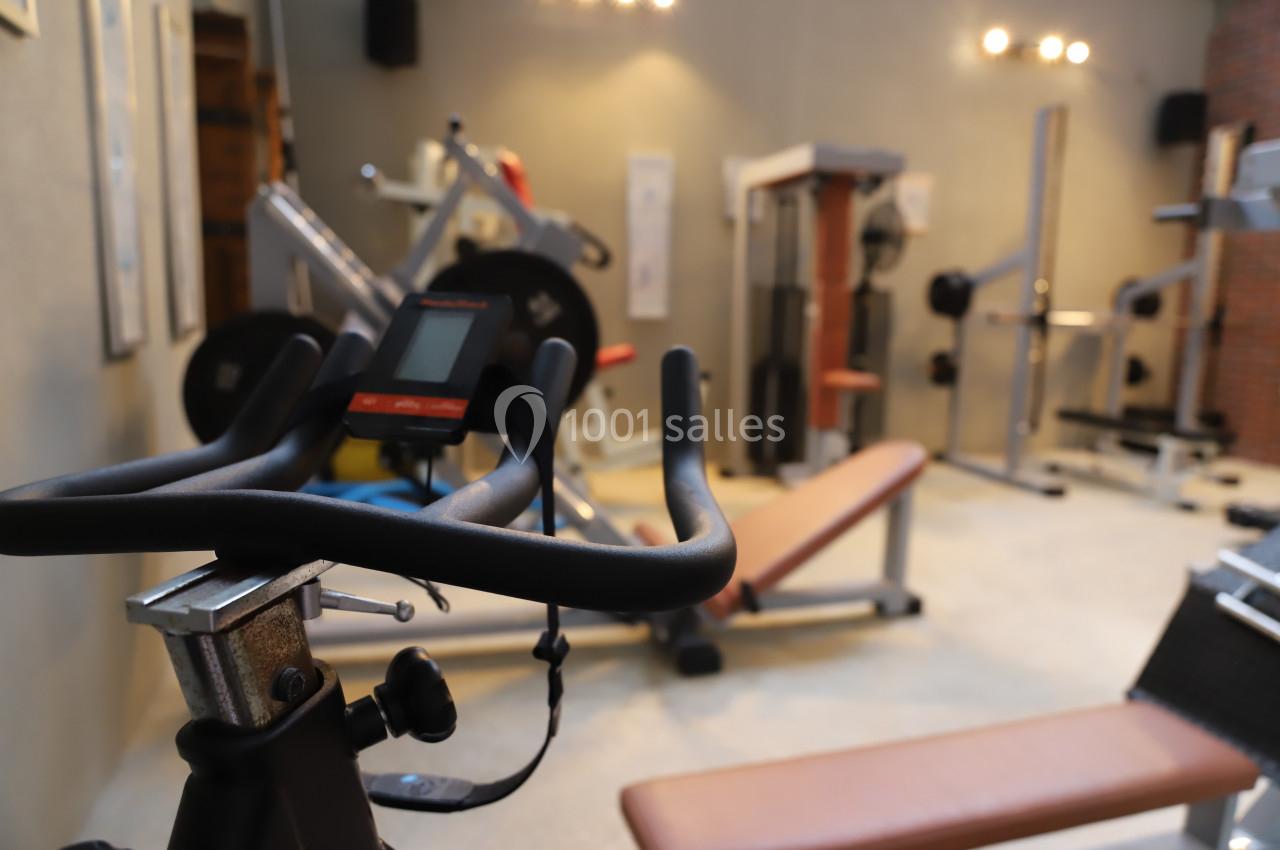 Salle de sport avec divers équipements de musculation et un vélo d'exercice au premier plan.