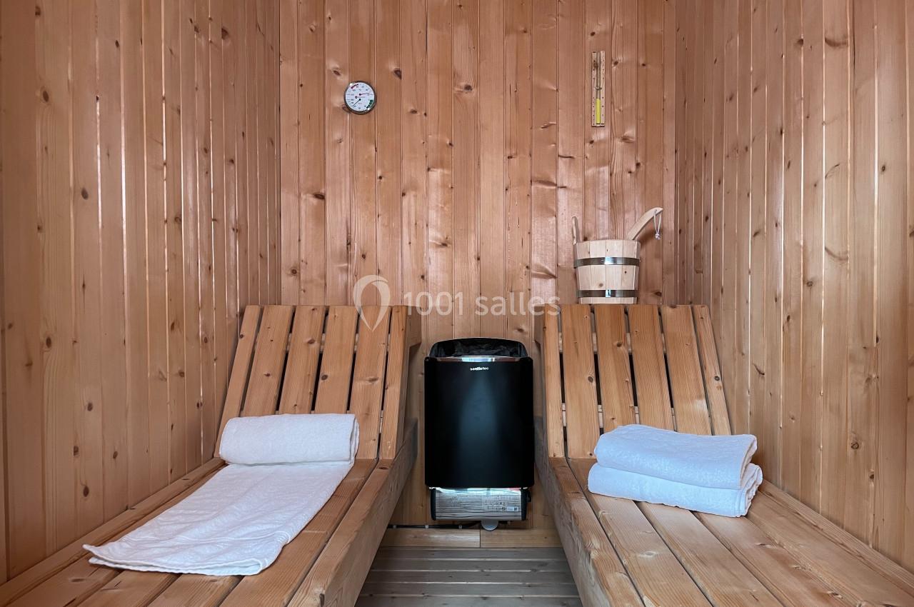 Intérieur d'un sauna en bois avec deux bancs, des serviettes pliées et un poêle central.