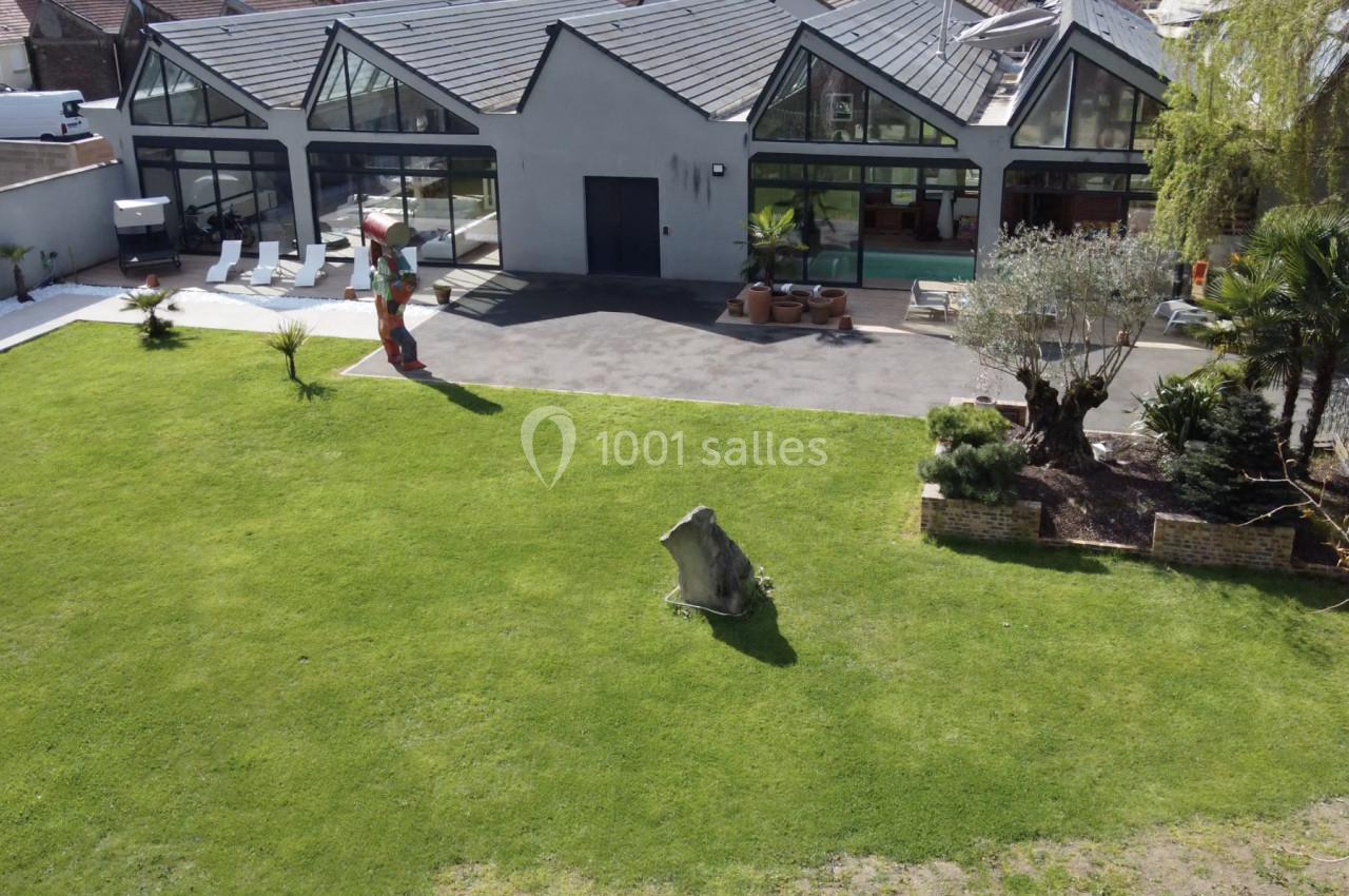 Vue aérienne d'une maison moderne avec grandes baies vitrées, jardin aménagé et pelouse entretenue.