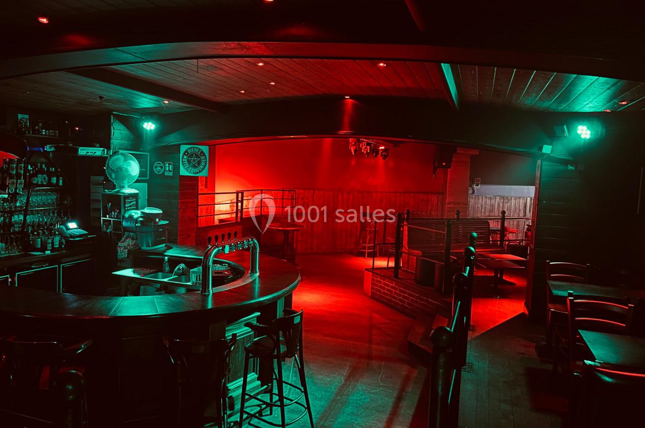 Intérieur d'un bar vide avec éclairage rouge tamisé, comptoir central et tables en arrière-plan.