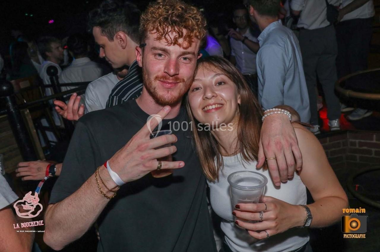 Un homme et une femme sourient à la caméra dans un environnement festif avec des lumières tamisées.