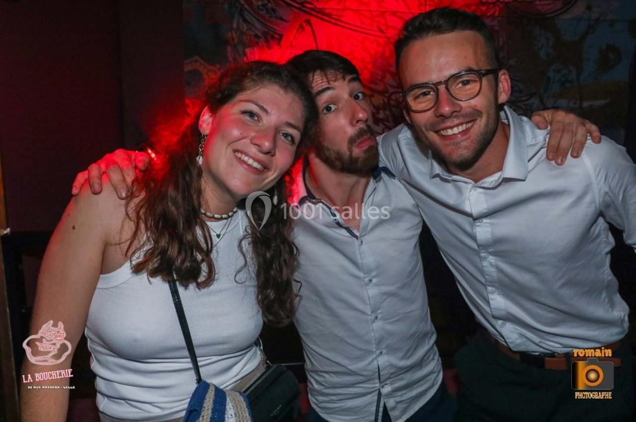 Trois personnes souriantes posant ensemble dans un environnement intérieur avec éclairage rouge.