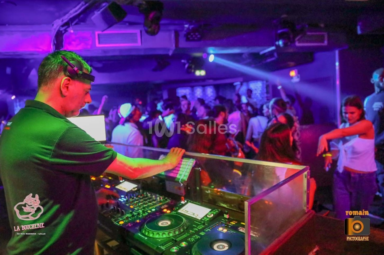 Un DJ mixe dans une boîte de nuit animée, avec une foule dansante sous des lumières colorées.