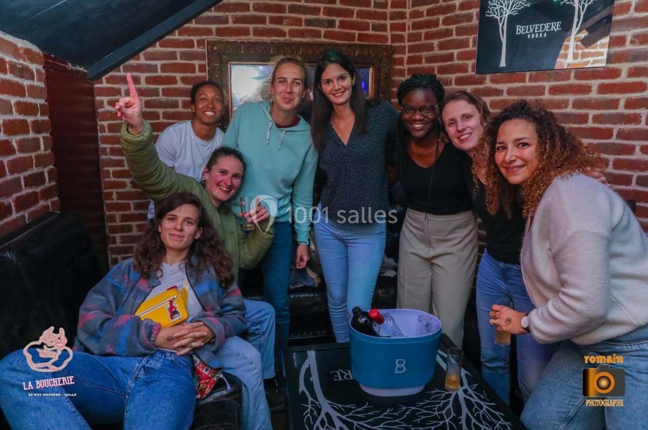 Un groupe de personnes souriantes posant dans un intérieur avec des murs en briques et un seau à boissons au centre.