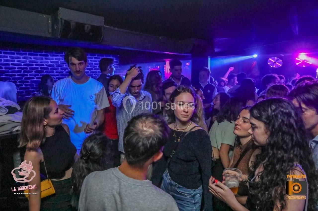 Groupe de jeunes discutant et dansant dans une ambiance de boîte de nuit avec éclairages colorés.