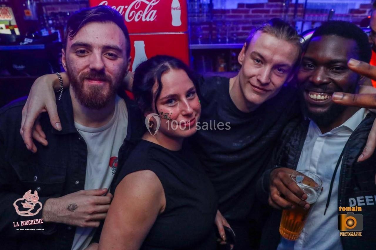 Quatre personnes souriantes posent dans un bar, avec des boissons et un décor lumineux en arrière-plan.