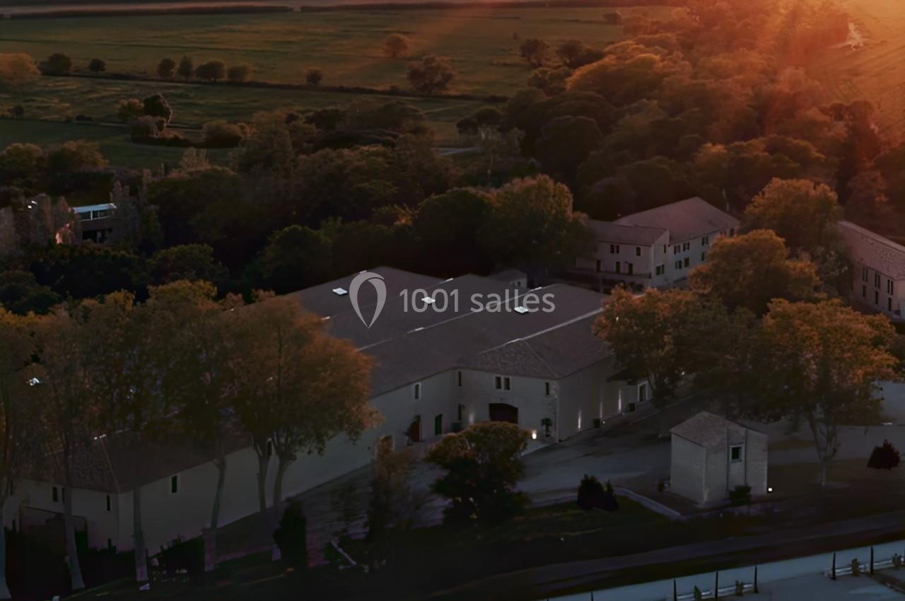 Vue aérienne d'un complexe de bâtiments entouré d'arbres et de champs au coucher du soleil.