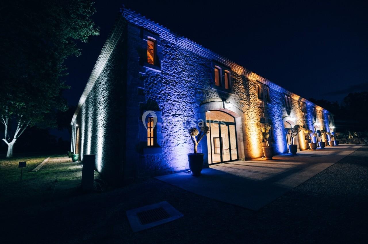 Façade d'un bâtiment en pierre éclairée par des lumières colorées bleues et jaunes, de nuit.