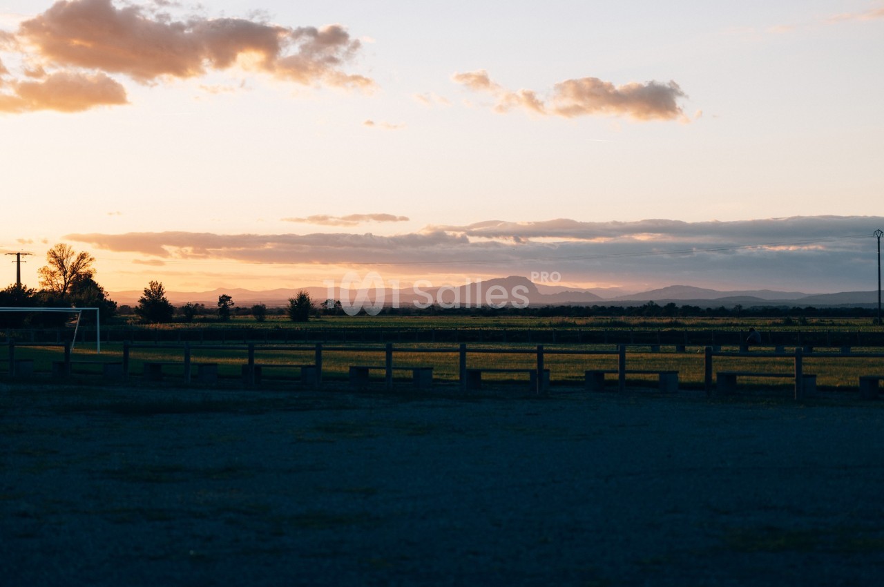 Paysage au coucher du soleil avec des champs, une clôture en bois et des montagnes à l'horizon sous un ciel partiellement…