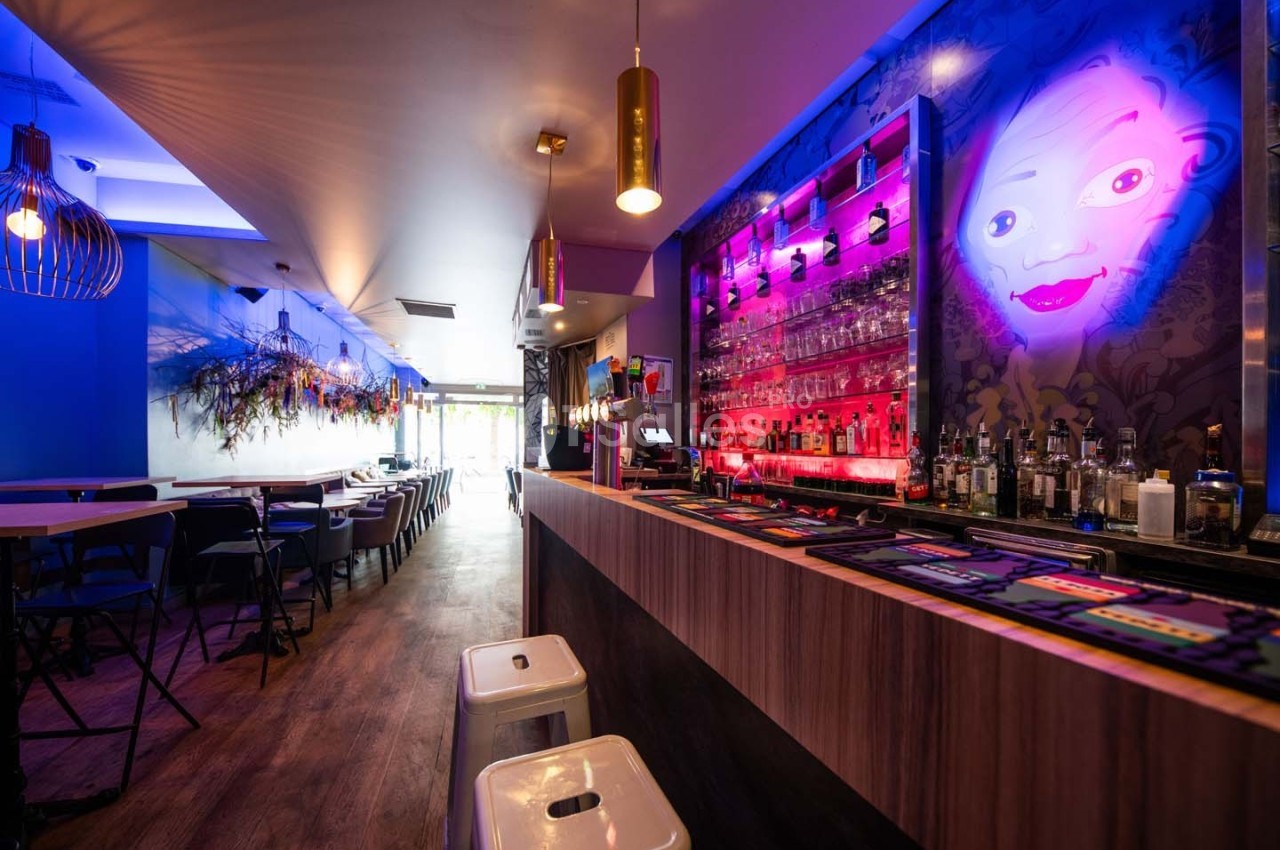 Intérieur d'un bar moderne avec un comptoir éclairé, des tabourets et une décoration murale colorée.
