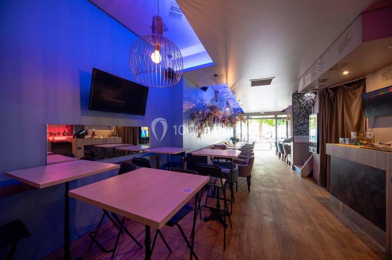 Salle de restaurant moderne avec tables en bois, éclairage tamisé et vue sur l'entrée lumineuse.