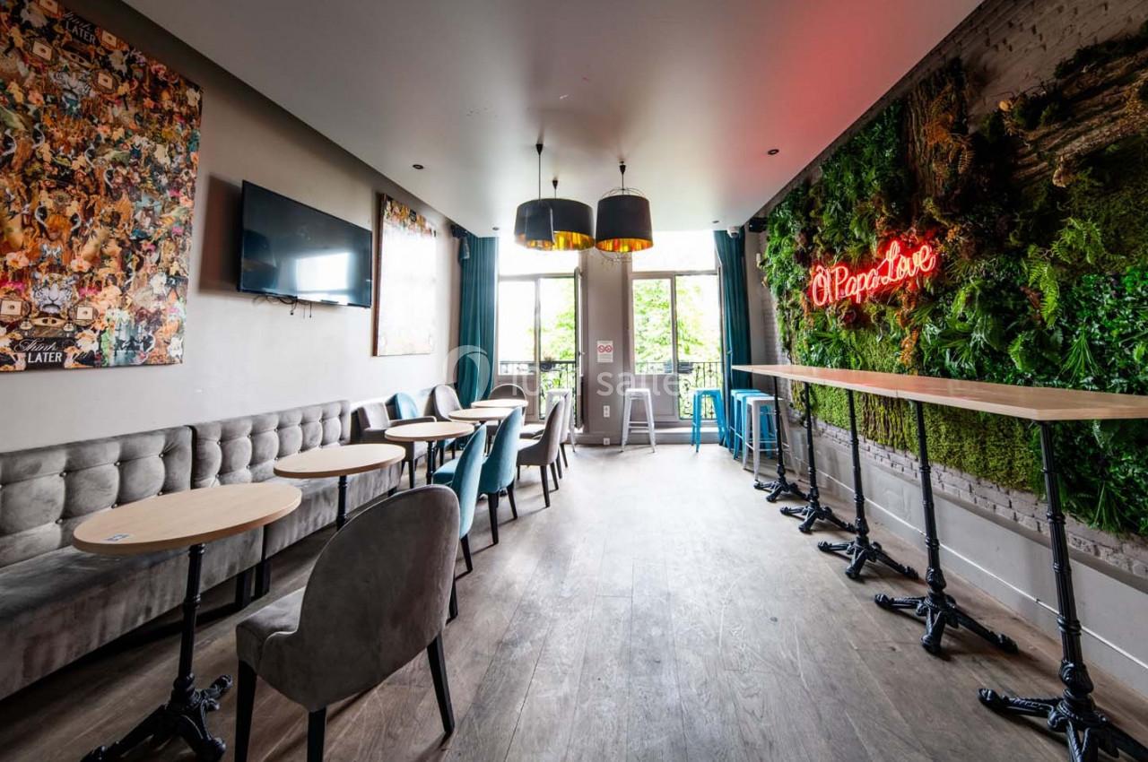 Salle lumineuse avec tables en bois, chaises modernes, mur végétal, néon rouge et grandes fenêtres donnant sur l'extérieur.
