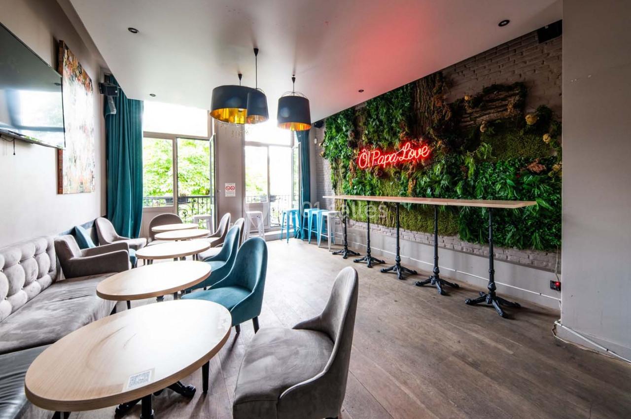 Salle lumineuse avec tables rondes, chaises modernes, mur végétal et enseigne néon rouge ’Pizza & Love’.