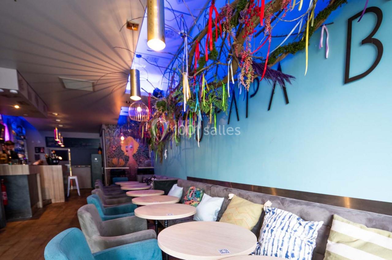 Salle de café moderne avec murs bleus, décoration florale suspendue et tables rondes entourées de fauteuils.