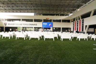 Table ronde en bois entourée de chaises à motifs rouges et blancs, située dans un jardin avec des plantes et des fleurs.