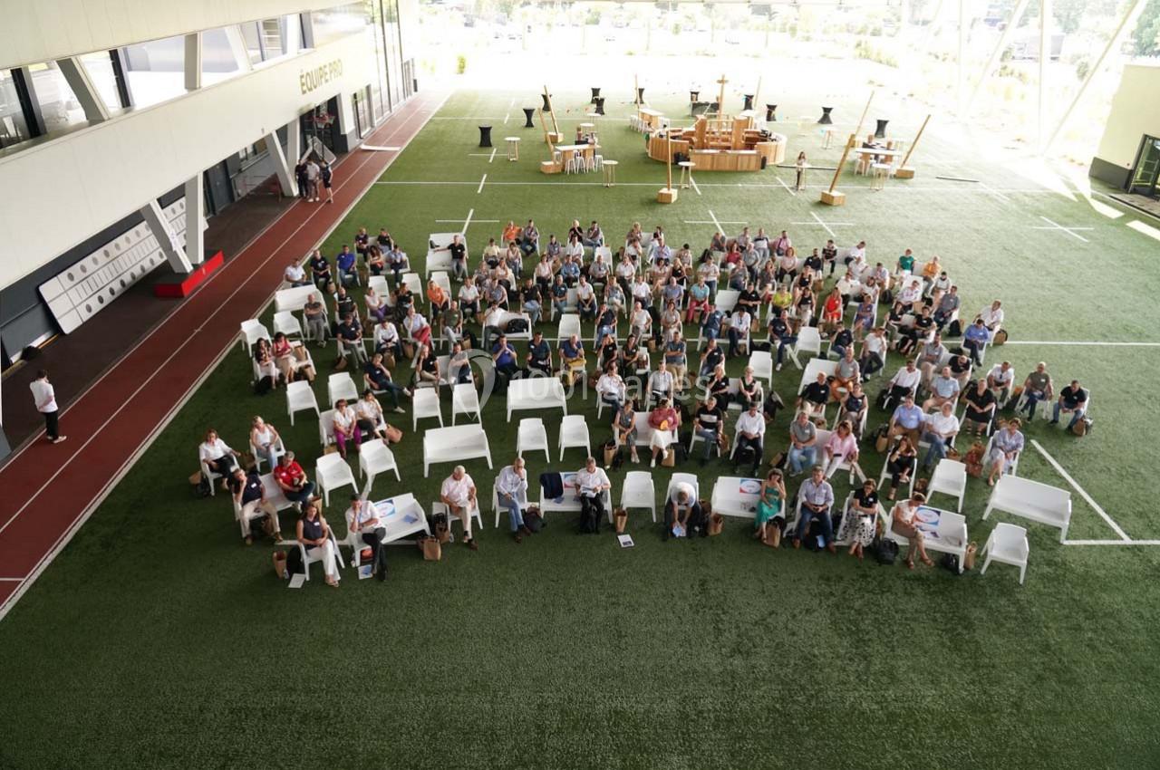 Vue aérienne d'un groupe de personnes assises sur des chaises blanches dans un espace intérieur avec sol en gazon…
