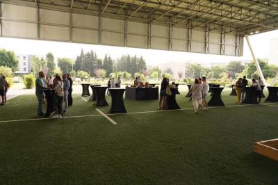 Table ronde en bois entourée de chaises à motifs rouges et blancs, située dans un jardin avec des plantes et des fleurs.