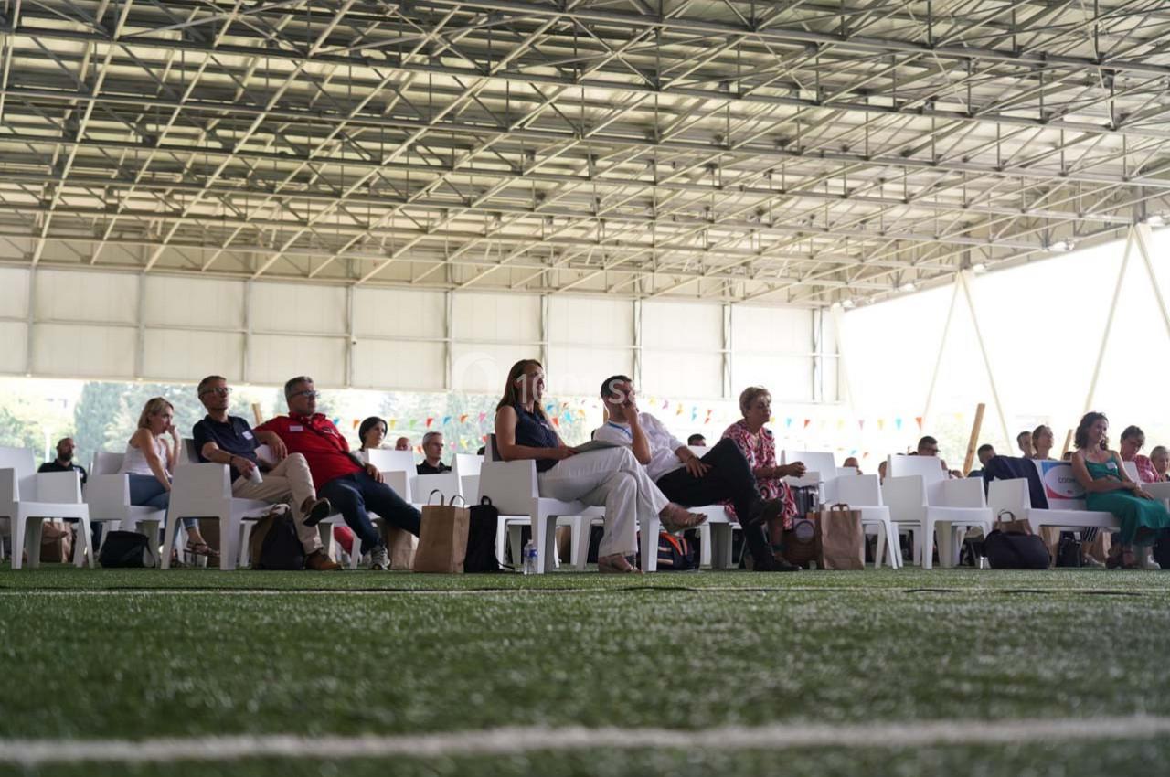 Des personnes assises sur des chaises blanches dans un espace couvert, avec un sol en gazon synthétique.