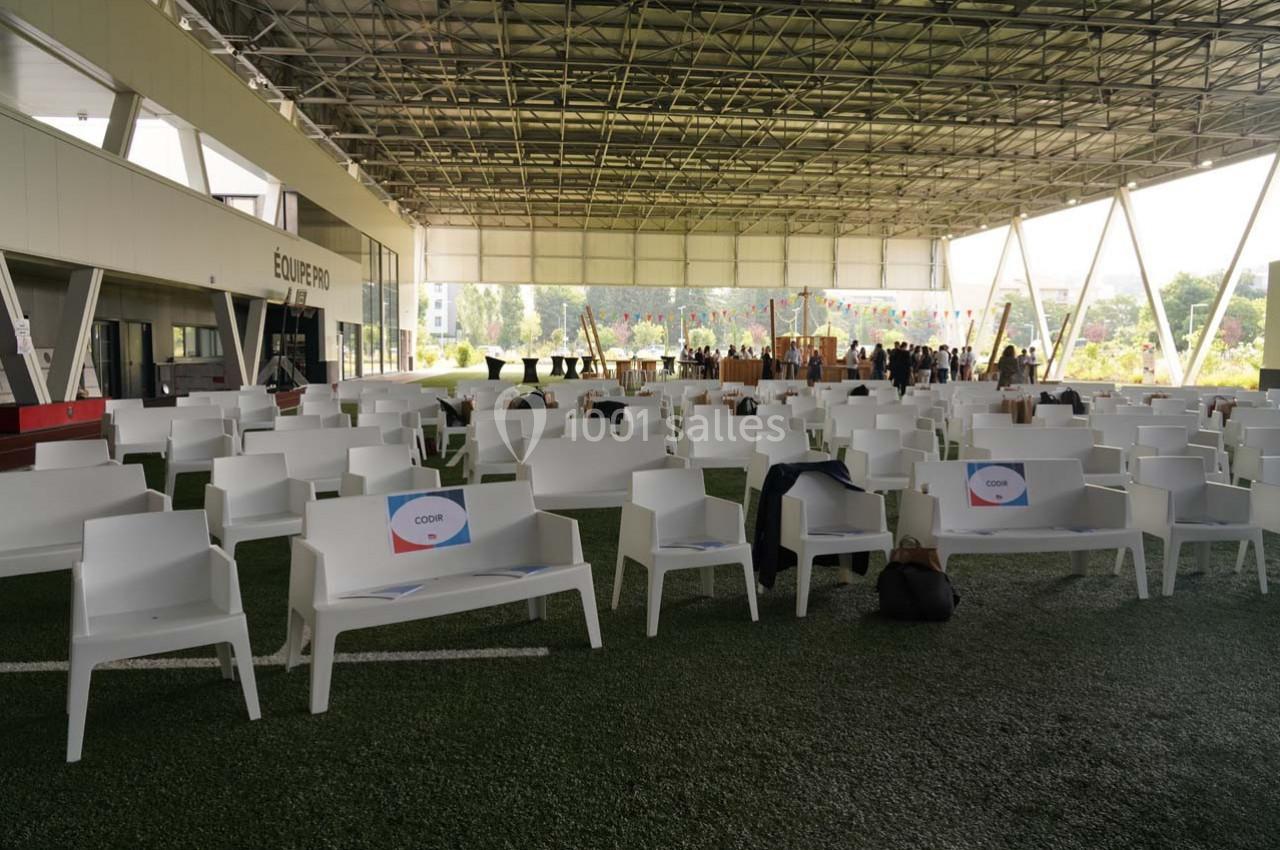 Chaises blanches alignées sous une structure couverte, avec des panneaux et une zone d'accueil en arrière-plan.