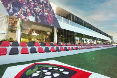 Table ronde en bois entourée de chaises à motifs rouges et blancs, située dans un jardin avec des plantes et des fleurs.