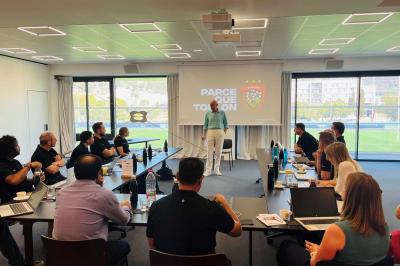 Table ronde en bois entourée de chaises à motifs rouges et blancs, située dans un jardin avec des plantes et des fleurs.
