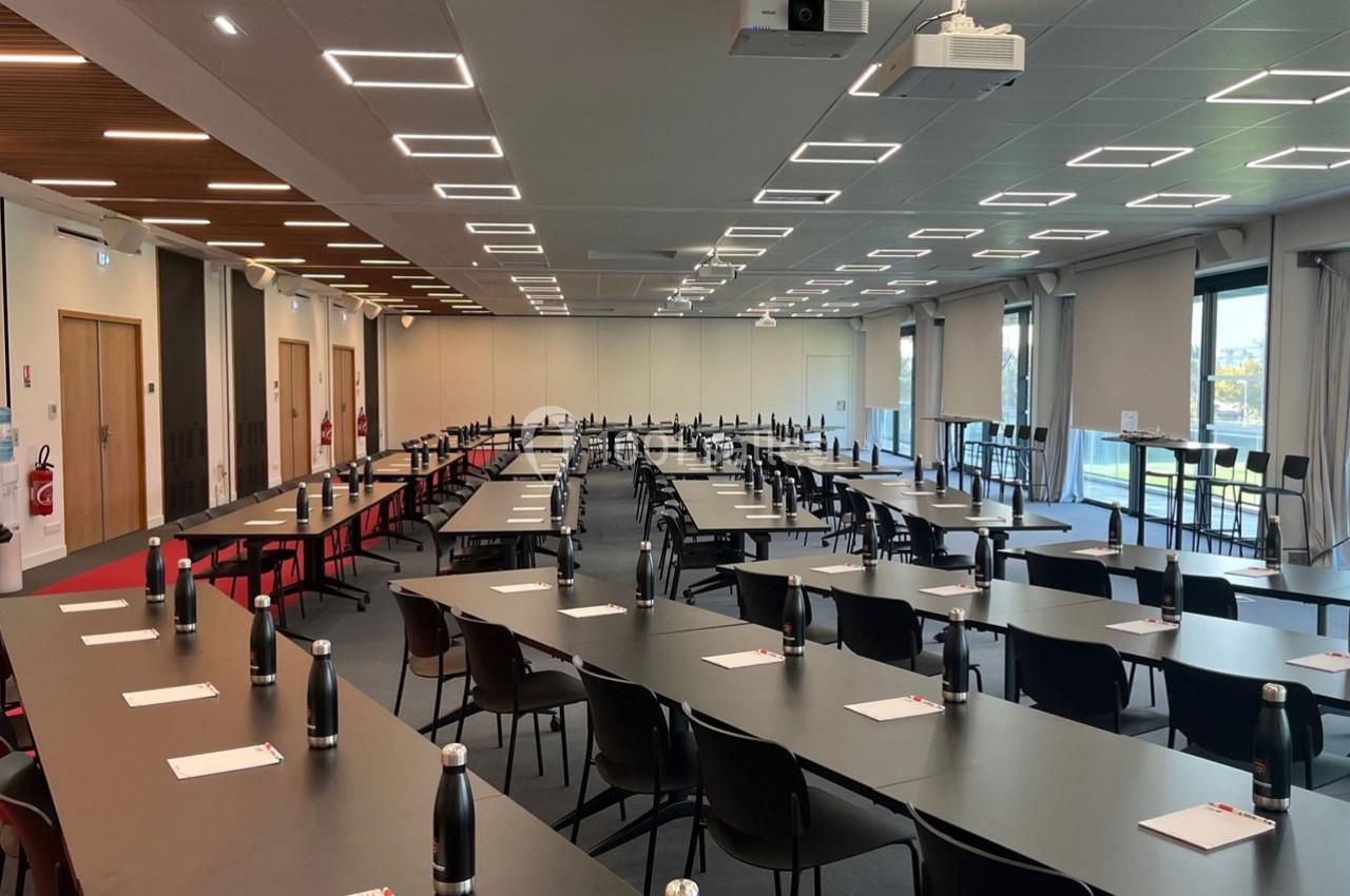 Salle de conférence moderne avec des tables en disposition en U, chaises alignées, bouteilles d'eau et blocs-notes.