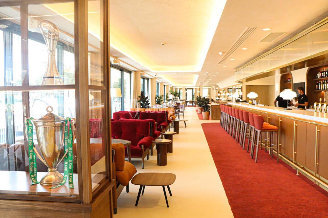 Intérieur d'un bar élégant avec un comptoir long, des fauteuils rouges, et un trophée exposé dans une vitrine.