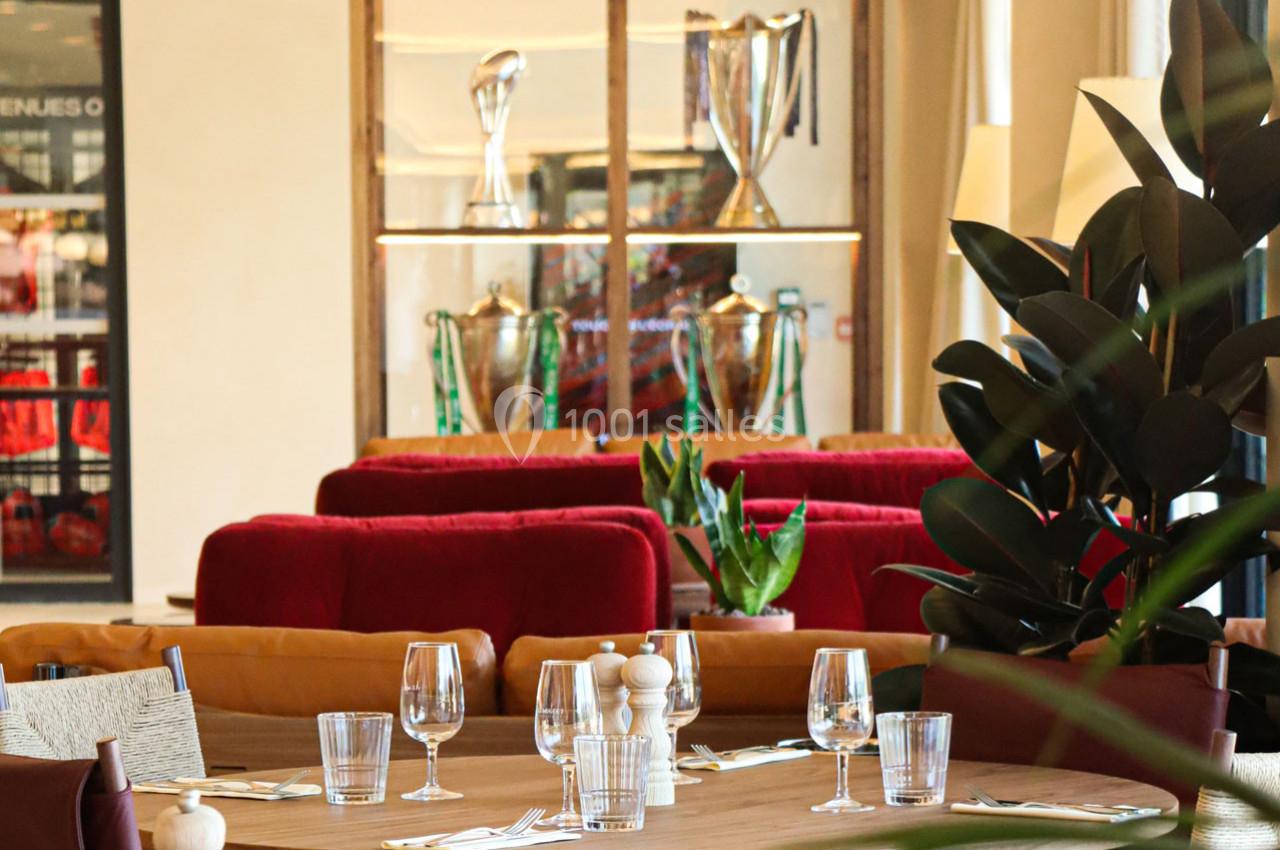 Salle de restaurant élégante avec tables dressées, plantes et vitrines exposant des trophées en arrière-plan.