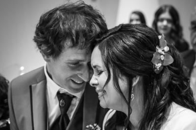 Un couple en tenue de mariage pose devant une voiture ancienne noire et un bâtiment historique entouré de verdure.