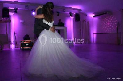 Un couple de mariés danse au centre d'une salle entourée d'invités, avec un sol recouvert de fumée légère.