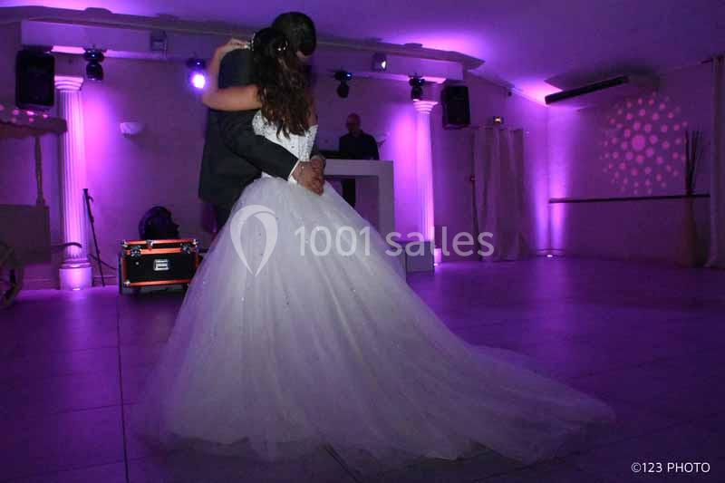 Un couple danse dans une salle éclairée par des lumières violettes, avec un DJ en arrière-plan.