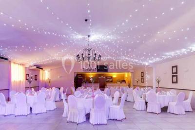 Un couple de mariés danse au centre d'une salle entourée d'invités, avec un sol recouvert de fumée légère.