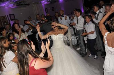 Un couple de mariés danse au centre d'une salle entourée d'invités, avec un sol recouvert de fumée légère.