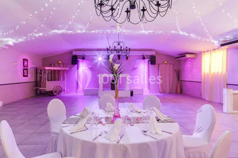 Salle de réception décorée avec des lumières suspendues, une table ronde dressée et un éclairage rose.