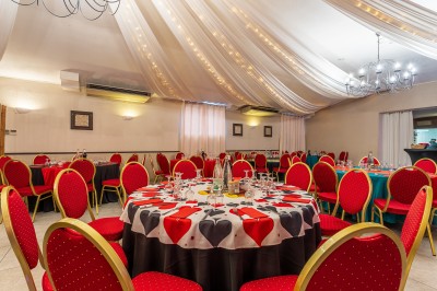 Salle de réception décorée avec des tables rondes dressées, chaises rouges et plafond drapé de voilages lumineux.