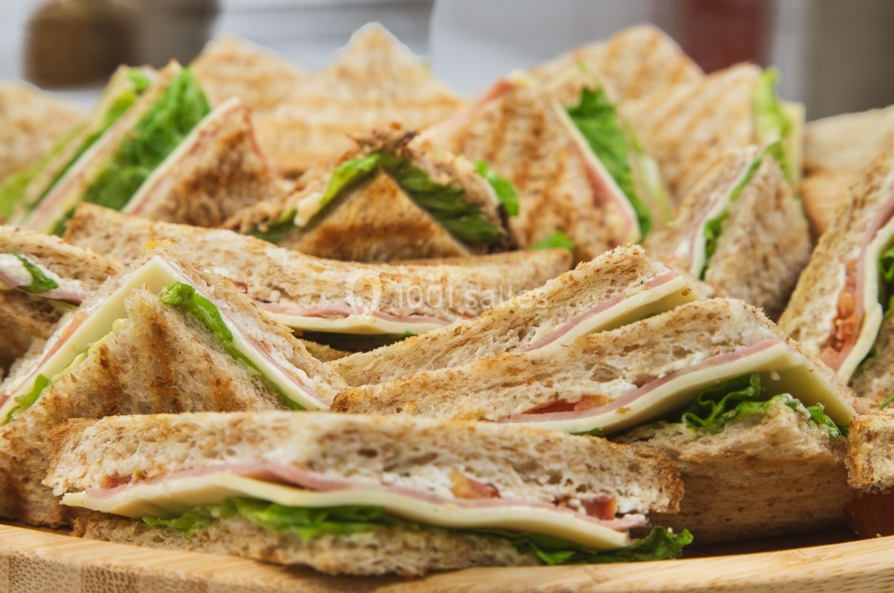 Assortiment de sandwichs triangulaires garnis de jambon, fromage, laitue et tomate sur un plateau en bois.