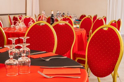 Salle de réception décorée avec des tables rondes dressées, chaises rouges et plafond drapé de voilages lumineux.