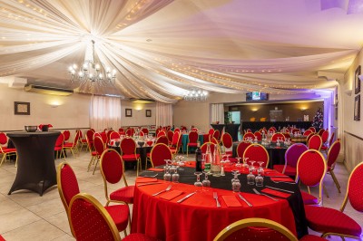 Salle de réception décorée avec des tables rondes dressées, chaises rouges et plafond drapé de voilages lumineux.