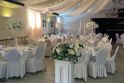 Salle de réception décorée avec des tables rondes dressées, chaises rouges et plafond drapé de voilages lumineux.