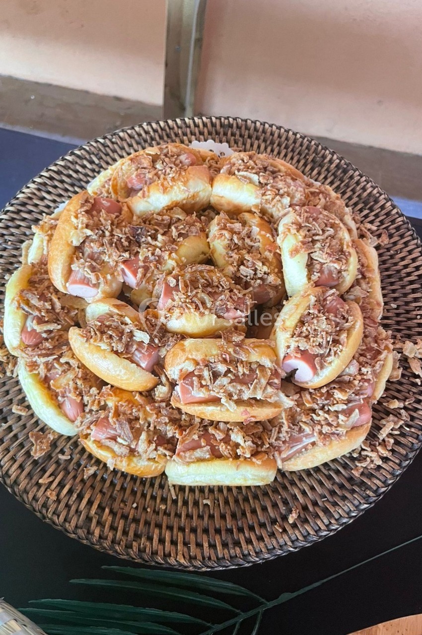 Plateau de petits pains garnis de jambon et d'oignons frits, disposés en cercle sur un panier en osier.